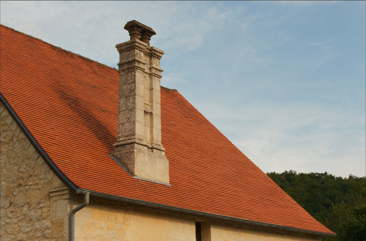 Couverture en tuiles plates du Périgord avec cheminée en pierre sculptée, réalisée par un couvreur en Dordogne — visuel d'illustration pour pose de tuiles à Périgueux
